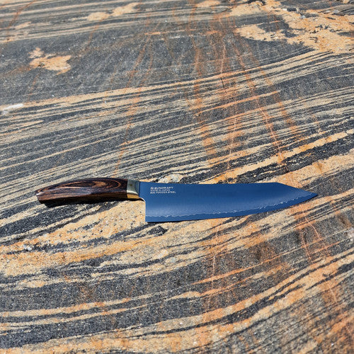 Alt-teksti: Tyylikäs kokkiveitsi sinisellä terällä ja puukahvalla kivipinnalla.