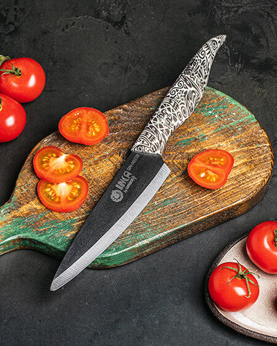 Alt-teksti: Tyylikäs keraaminen veitsi leikkuulaudalla viipaloimassa tomaatteja.