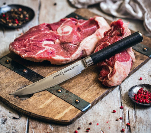 Alt-teksti: Tyylikäs Damascus-pihviveitsi ja raakaa lihaa puulevyllä