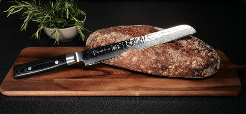 Alt text (in Finnish): Tyylikäs sahalaitaveitsi ja rapeakuorinen leipä leikkuulaudalla.