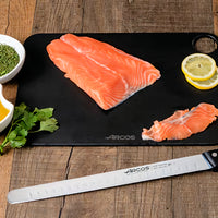 Arcos lohiveitsi 30 cm leikkuulaudalla lohifileen vieressä. Ovaalihionta ja taipuisa terä takaavat tarkan leikkuun.