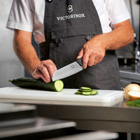 Kokki käyttää Victorinox Santoku veistä 17 cm Fibrox-kahvalla kurkun viipalointiin, osoittaen veitsen tarkkuuden ja käyttömukavuuden.