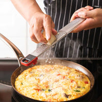 Cuisipro SGT Deluxe Dual Raastin käytössä juuston raastamiseen kuuman munakkaan päälle, monipuolinen keittiöväline ruoanlaittoon.