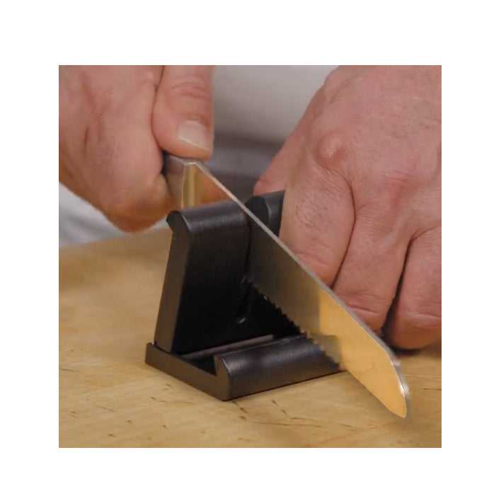 Retkiteroitin Basic Musta käytössä teroittamassa sahalaitaista veistä puisella alustalla. Kompakti käsiteroitin kotiin ja retkelle.