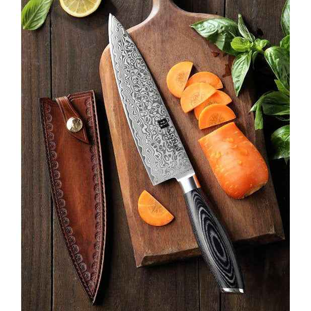 Xinzuo Ya Damascus kokkiveitsi leikkuulaudalla porkkanaviipaleiden kanssa, mukana koristeellinen nahkatuppi säilytykseen.