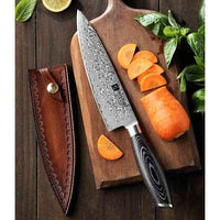 Xinzuo Ya Damascus kokkiveitsi leikkuulaudalla porkkanaviipaleiden kanssa, mukana koristeellinen nahkatuppi säilytykseen.