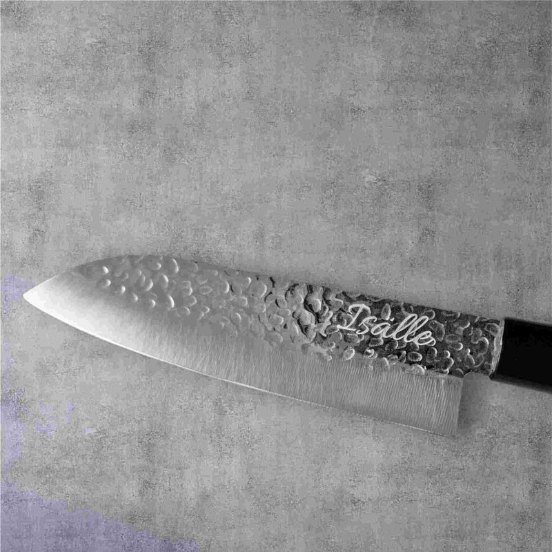 Japanilainen Santoku-veitsi, jossa on vasaroitu terä ja kaiverrettuIsalle"-teksti, harmaalla kivimäisellä taustalla.