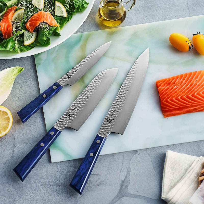 Yaxell Blue Breeze keittiöveitset, mukaan lukien 13 cm vihannesveitsi, esillä leikkuulaudalla kalan ja vihannesten kanssa.