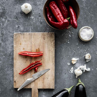 Global GS-1 kuorintaveitsi leikkuulaudalla punaisten chilien, valkosipulin ja munakoison kanssa – japanilainen ruostumaton teräsveitsi