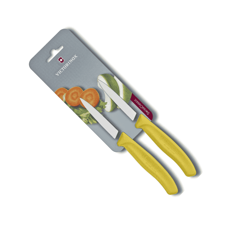 Victorinox Kuorimaveitsi Setti - 8 cm, 2 kpl Swiss Classic keltaisella kahvalla, pakkauksessa vihanneksia taustalla. Täydellinen juuresten kuorintaan.