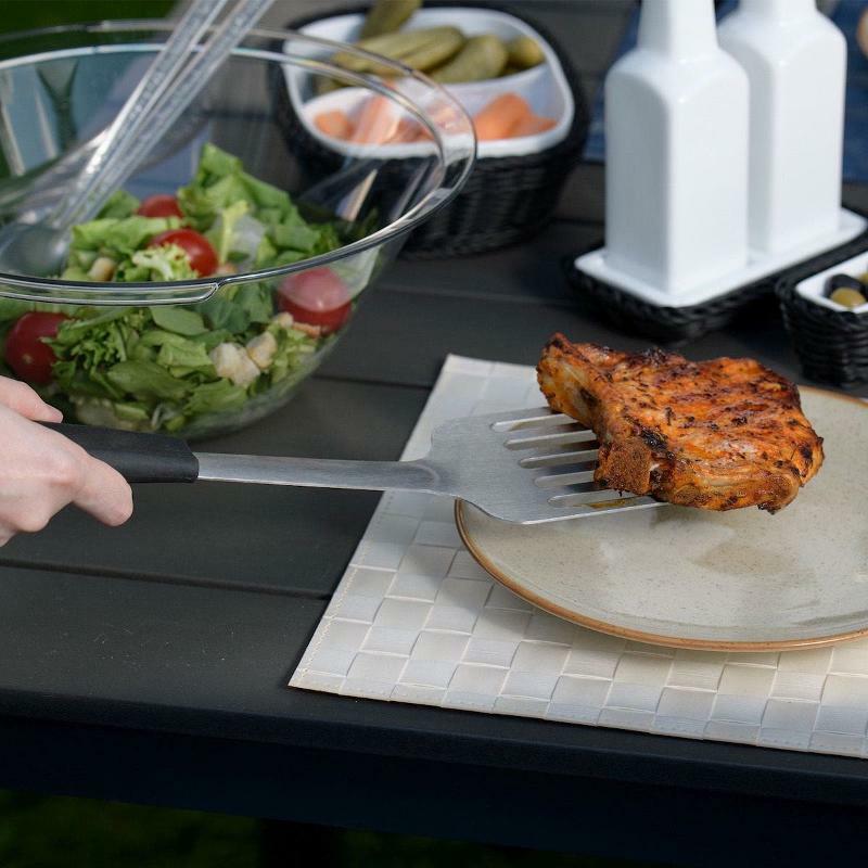 Westmark grillilasta käytössä ulkogrillauksessa, nostamassa grillattua lihaa lautaselle puutarhapöydällä.