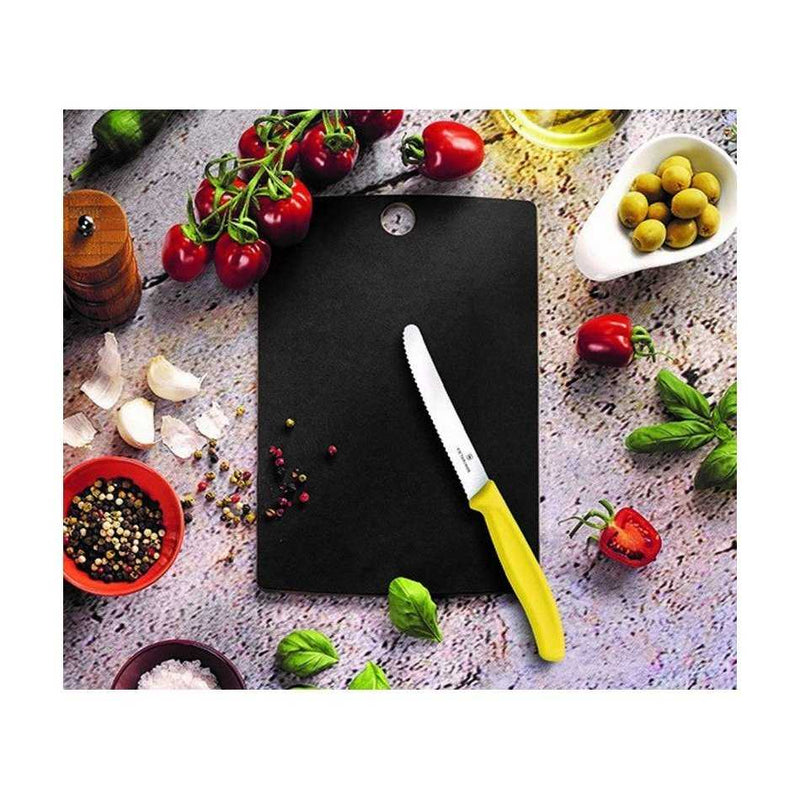 Victorinox Puukuitu Leikkuulauta S musta käytössä keittiössä, leikkuuveitsi ja tuoreita raaka-aineita leikkuulaudan ympärillä.