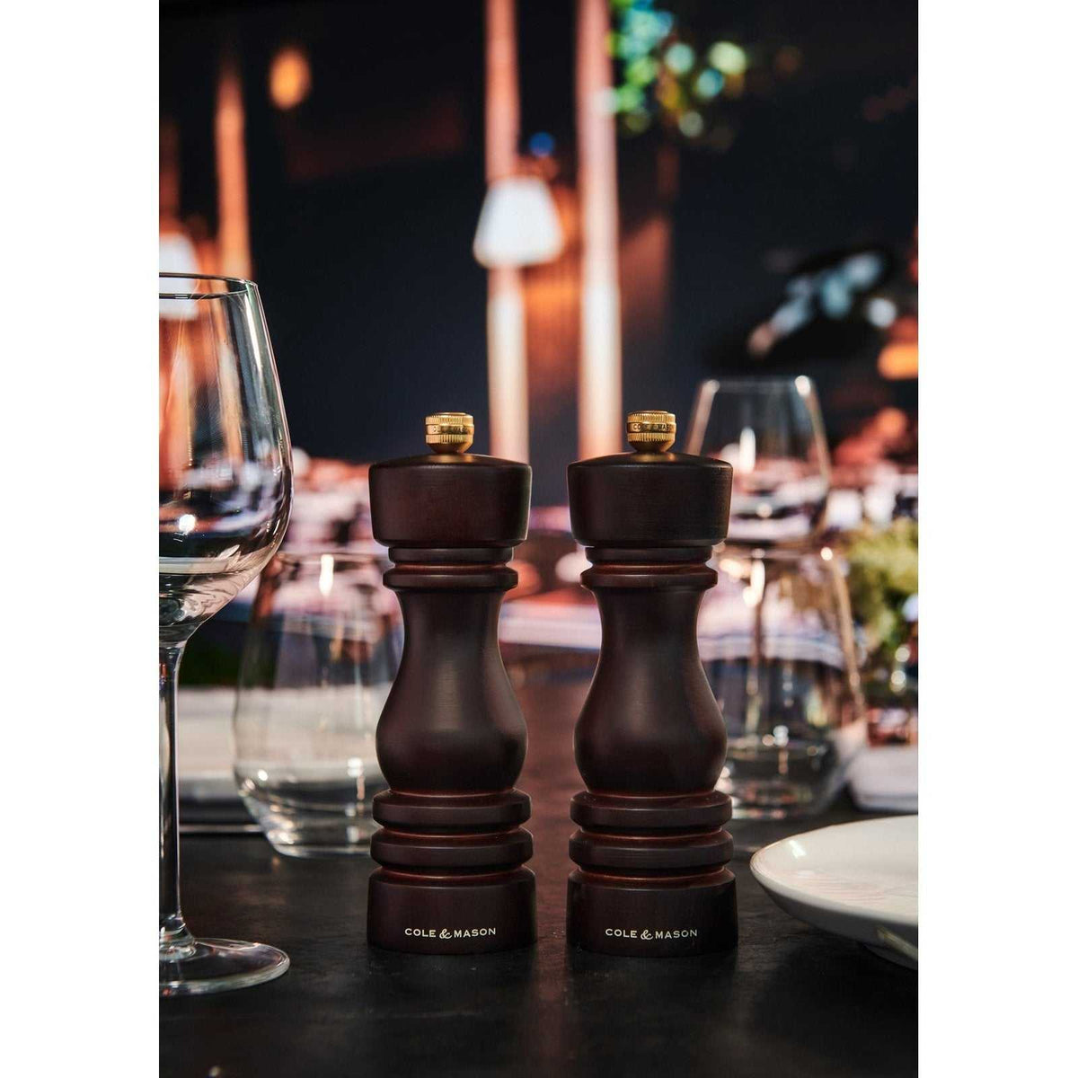 London Suolamylly ja pippurimylly ruokapöydällä, elegantti tumman ruskea muotoilu, taustalla kattaus.